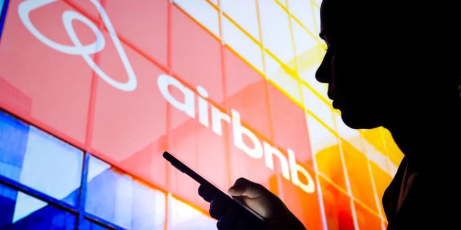 BBC Mundo: Sombra de una mujer sosteniendo un teléfono y con el logo de Airbnb detrás.