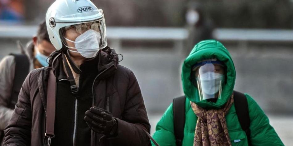 BBC Mundo: Un hombre con casco y mascarilla n95 camina por las calles y una mujer con mascarilla y careta detrás de él.